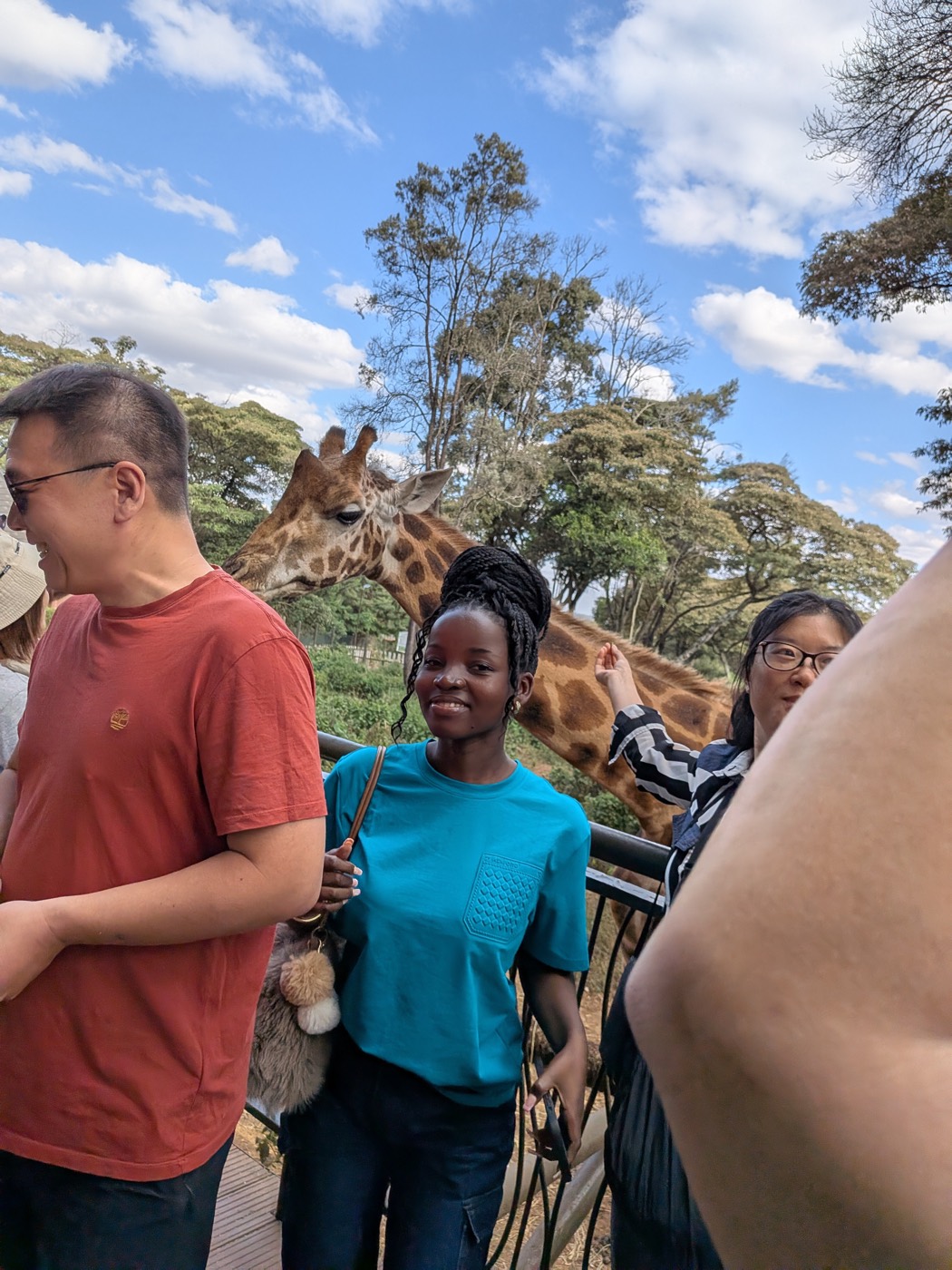 Travelers smiling with a giraffe behind them